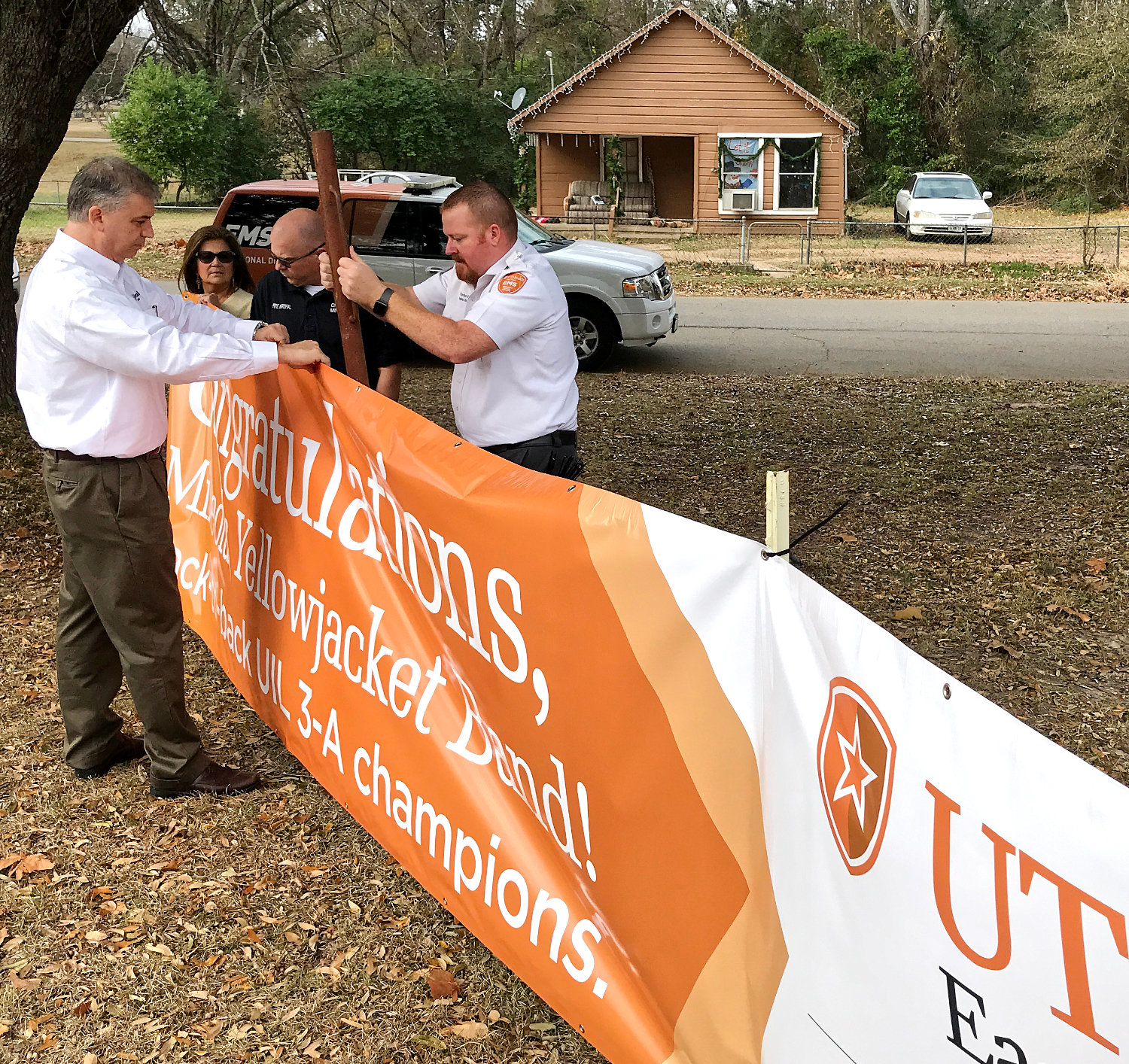 Scott Berkley, left, and Hayden Ray, right, with UT Health, are assisted by Mineola City Manager Mercy Rushing and Fire Marshal David Madsen installing a new banner proclaiming the Mineola High School Sound of the Swarm marching band as back-to-back state champions, along side the state championship sign off Hwy. 69 South.